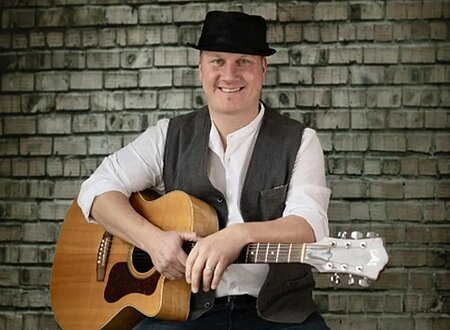 Ein Mann mit Gitarre sitzt auf einem Barhocker