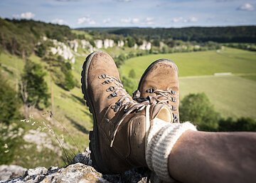 Braune Wanderschuhe mit hellen Socken sind im Mittelpunkt. Dahinter erstrecken sich die zwölf Apostel, die am Altmühltal-Panoramaweg liegen.